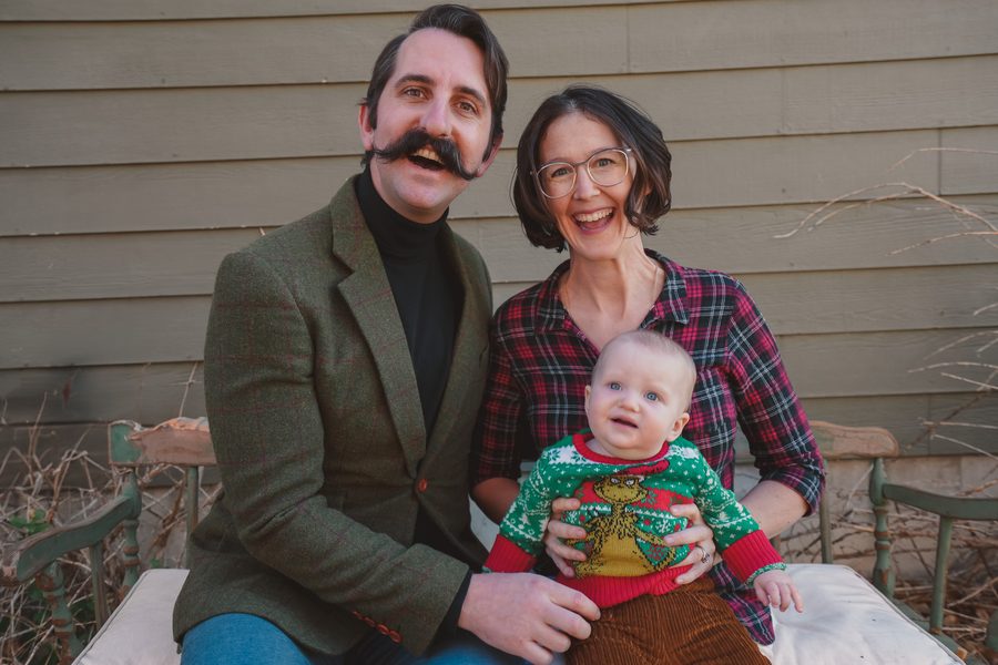 Laughing parents on a vintage green bench with their baby in a holiday sweater