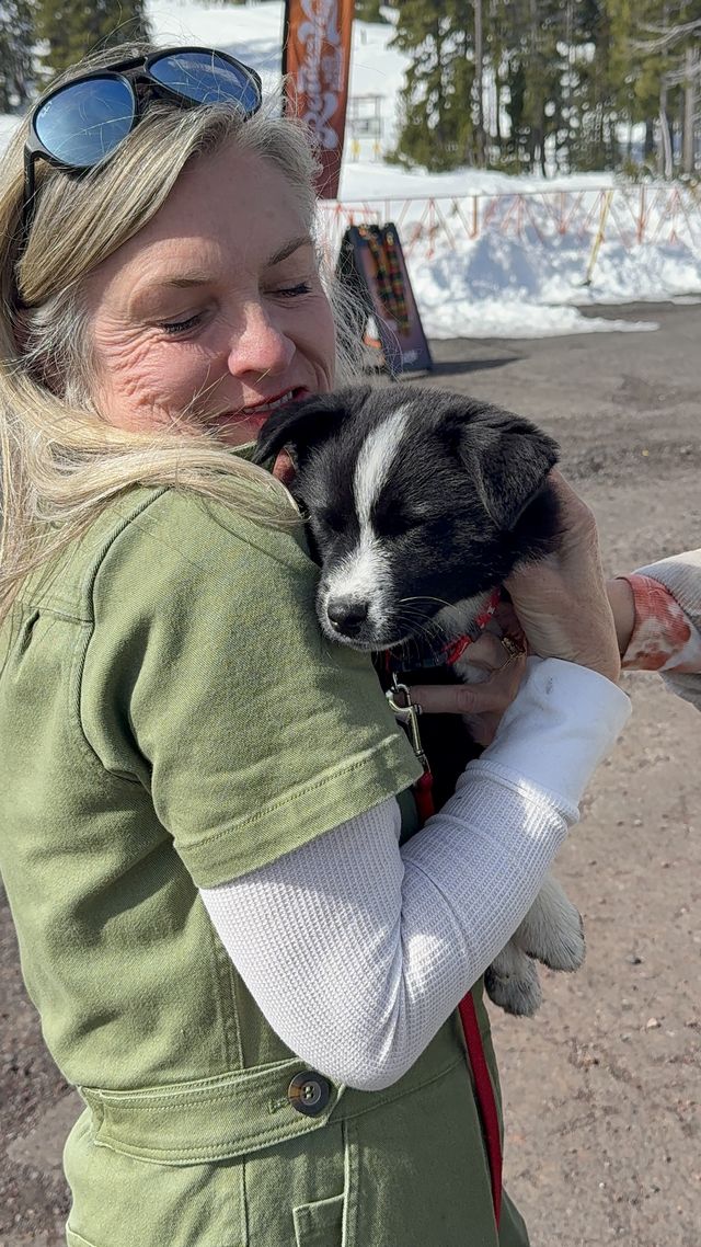 A woman with her eyes closed snuggling a sleepy black-and-white puppy against her shoulder
