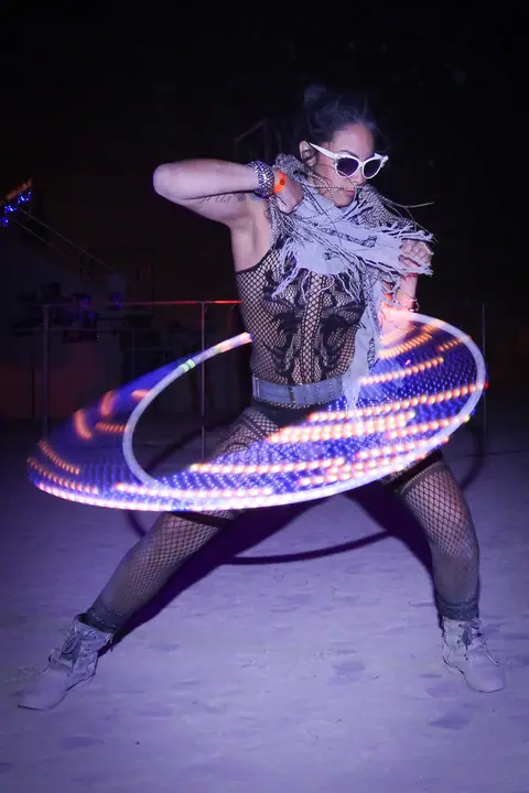 A performer spinning a glowing LED hoop, leaving purple light trails at night