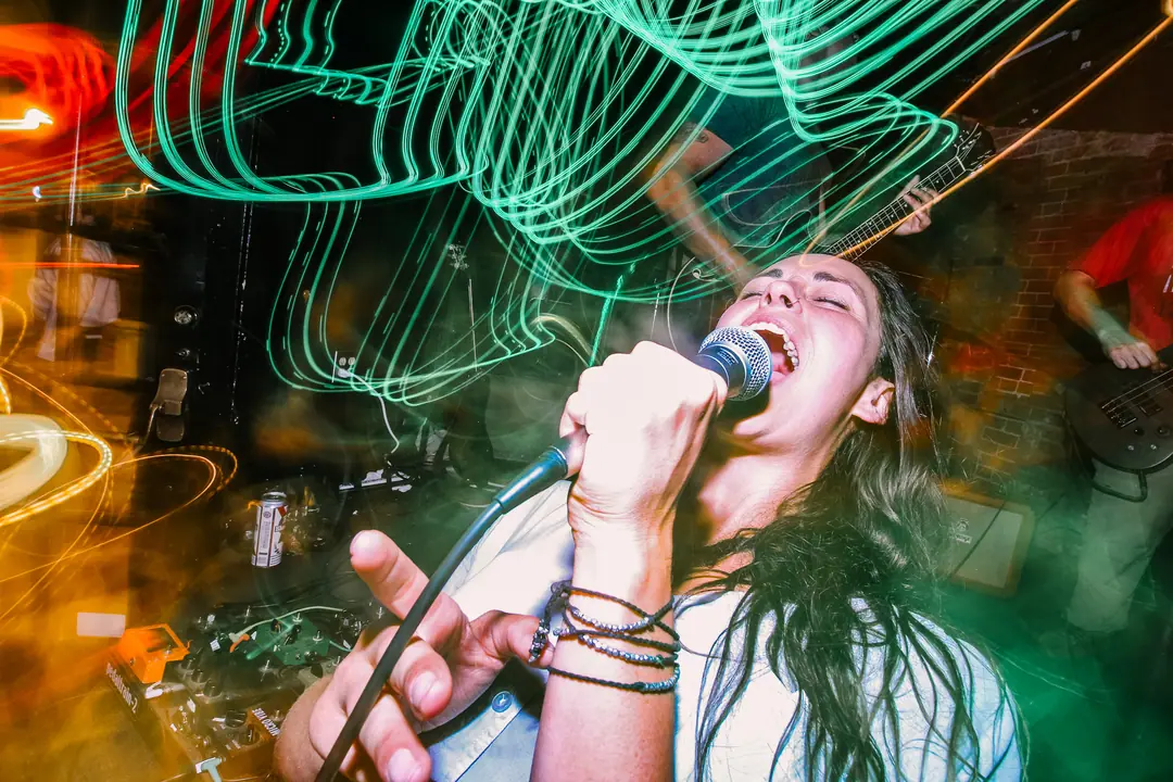 A singer belting into a microphone, surrounded by green neon light trails