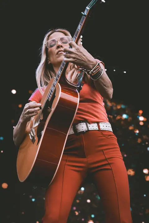 A festival guitarist performing in a bright outfit under colorful stage lights