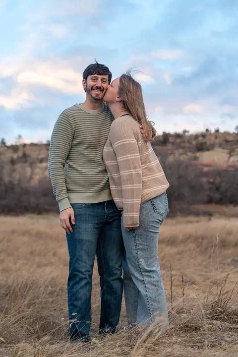 A couple embracing in a golden field, one planting a kiss on the other's cheek