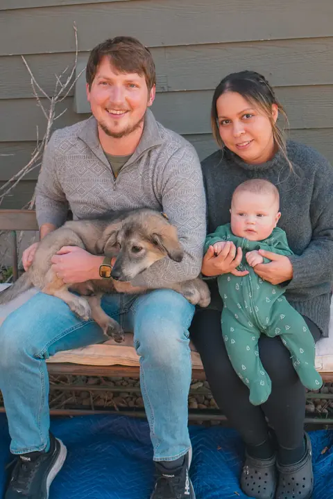 A couple on a bench holding their baby and a fluffy puppy