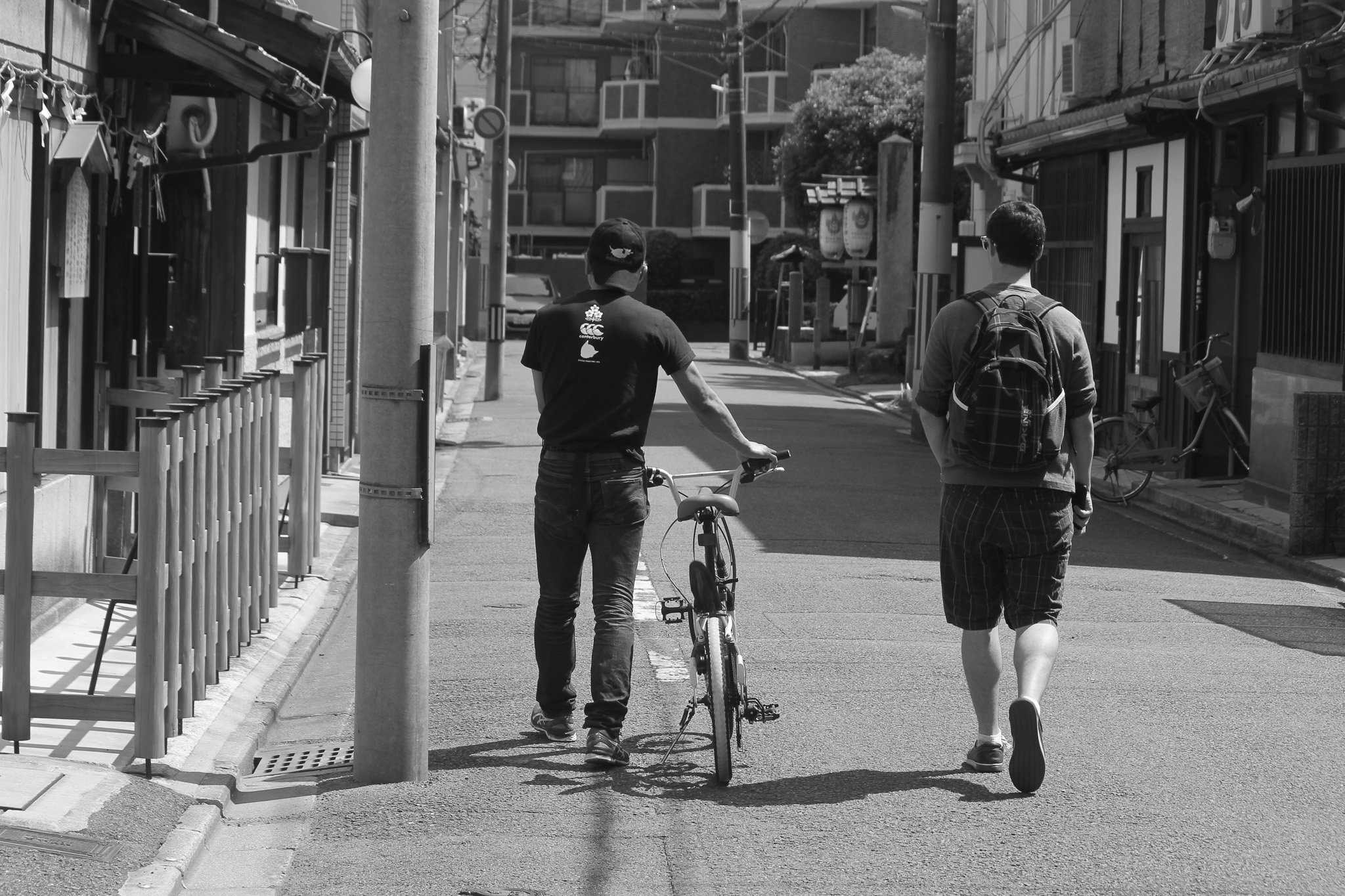 Two people walking through a neighborhood street in Japan, one beside a bicycle